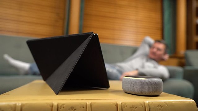 Man, lying on the couch, watching movie on Amazon Fire HD tablet, Echo Dot blinks yellow