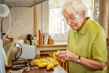 Elderly Woman in the Kitchen Peeling Potatoes