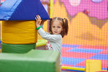 Image of little cute caucasian girl with ponytail playing with soft building blocks, child wearing...