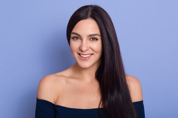 Fototapeta premium Image of young beautiful gorgeous young woman with perfect skin wearing dark blue dress posing with bare shoulders. Beauty fasion and care concept, attractive girl looks smiling directly at camera.
