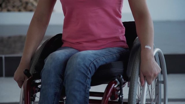 Adult disabled female in denim jeans and casual wear sitting in comfort handicap in house with soft natural daylight room. Woman in comfort wheelchair spin around on holding hands on wheel