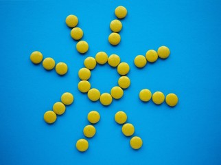 Yellow shape of sun made of candy, on blue solid background with copy space.