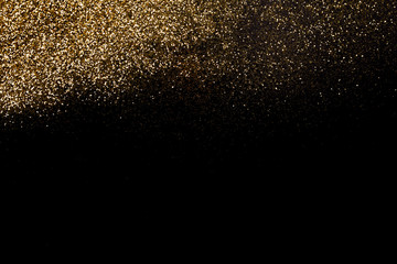 Golden glitter dispersed on a deep black surface. Christmas, new year, birthday, special occasions background, with a copy space.
