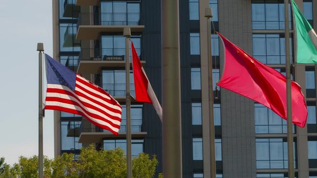A backlit American flag, Canadian flag, Chinese flag, and Irish flag, blowing in the wind with a building in the background.
