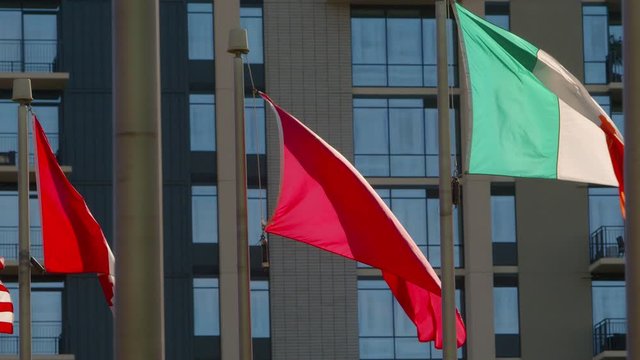 A backlit Canadian flag, Chinese flag, and Irish flag, blowing in the wind with a building in the background.