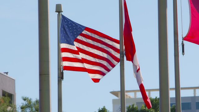 A backlit American flag, Canadian flag, Chinese flag, and Irish flag, blowing in the wind with a building in the background.