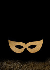 Golden carnival mask on black background with shiny, scattered glitter and a text space. Entertainment, costume, New Year's party.