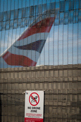 A drone prohibition sign on a security fence with the tail of a Boeing 787 Dreamliner in the background