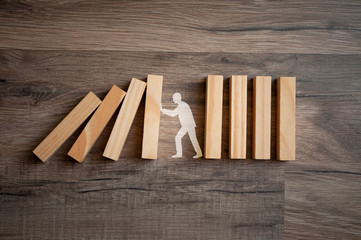 Wooden pieces with stick figure metaphor for stopping domino effect on wooden background