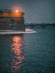 Winter night cityscape in St. Petersburg. The light of the lantern is reflected in the water of the river.