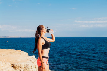 Fototapeta na wymiar Fitness girl drinking water from a shaker after a workout on the beach