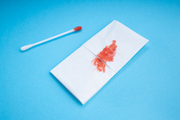 Blood on the paper napkin and cotton stick. Skincare mockup for design. Stack of disposable napkins on a blue background. Cosmetology concept. Bloody wound. Menstruation.