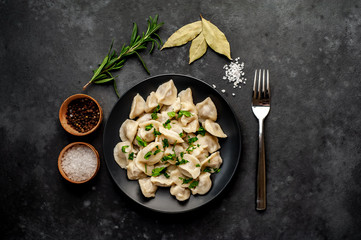 Dumplings - with spices and herbs in a black plate on a stone background. Traditional Russian dish - dumplings