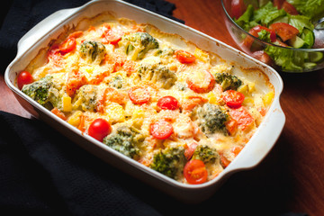 Ready-made baked vegetables in a white ceramic bowl with grated cheese and tomatoes. Natural style