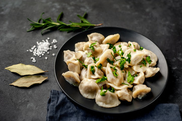 Dumplings with spices and herbs on a stone background with copy space for your text. Traditional Russian dish - dumplings