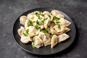 Dumplings - with spices and herbs in a black plate on a stone background. Traditional Russian dish - dumplings