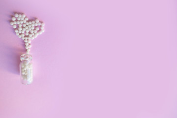 Heart made of homeopathic globules and glass bottle on pink background. 
