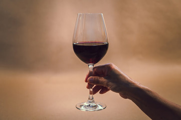 Hand holding glass of red wine with rustic background