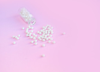 Homeopathy globules in glass bottles on a pink background. Alternative homeopathy herbal medicine, pills. Copyspace for text.
