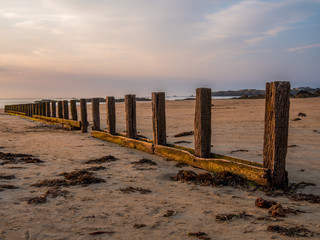 A wooden breakwater on the sand beach at the beautiful sunset.