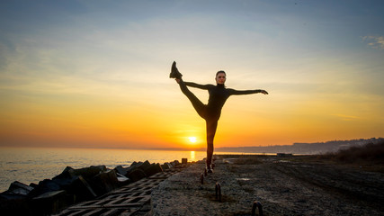 Young woman silhouette practicing yoga on the sea beach at sunset