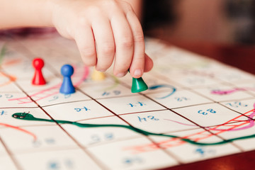 Kids hand with green chip under the board game, close up. Hand-drawn game Snakes and Ladders.