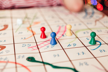 Hand-drawn game Snakes and Ladders. Colored chips on the field. Close-up. Christmas tree in the background