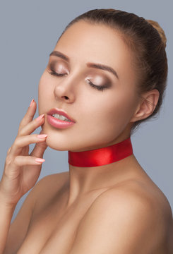 Portrait Of A Beautiful Happy Woman With Beautiful Fresh Nude Make-up, Thick Eyebrows And With Clean Skin In A Beauty Salon.She Has A Red Ribbon Around Her Neck. Face Close-up. Make-up Concept