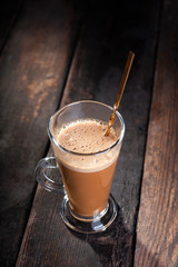 cappuccino in a glass cup with a spoon for cappuccino stands on an old shabby wooden background