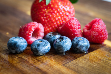 Fototapeta na wymiar Kitchen still life. Blueberries, raspberries and strawberries on a wooden board, kitchen concept healthy fresh food, newly washed, water on the board