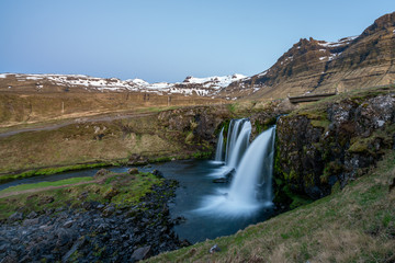 Kirkjufellsfoss at blue hour with snow covered mountains in the background. Traveling and icelandic landscape concept.