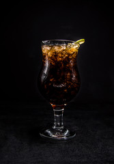 whiskey and coke cocktail with a slice of lime. a glass with a drink on a black, isolated background.