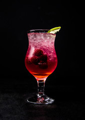pink cocktail with berries, ice and lime, on a black, isolated background.