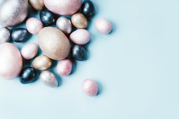 Colored painted pearl chicken and quail eggs of pink, silver, golden and blue color on a light blue pastel background. Minimalistic creative classic easter festive flat lay. Copyspace for text