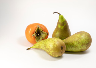 Ripe juicy orange persimmon and three Mature green pears lie on the table on a light gray background. Selective focus.