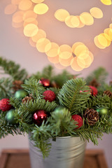 Fototapeta na wymiar Small arrangement of fresh spruce in a metal pot. Christmas mood. Bokeh of Garland lights on background.