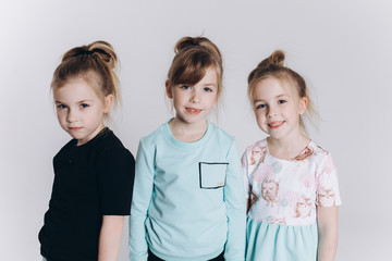 Happy cute adorable blondie triplets girls posing in studio together on isolated background. Childhood, children, twins concept. Smiling girls playing together
