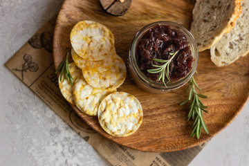 Fresh homemade chicken liver pate and onion chutney (marmalade) in a jar, bread and crackers on a wooden plate. Light grey background, selective focus.