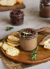 Fresh homemade chicken liver pate and onion chutney (marmalade) in a jar, bread and crackers on a wooden plate. Light grey background, selective focus.