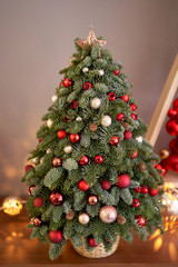 Beautiful small Christmas tree on wooden table. Happy mood. Garland lamp bokeh on background. Wallpaper. Danish pine and fir, Nobilis
