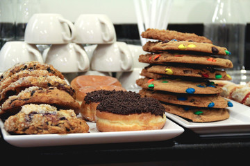 Scones, donuts, and cookies stacked in front of mugs in a coffeeshop
