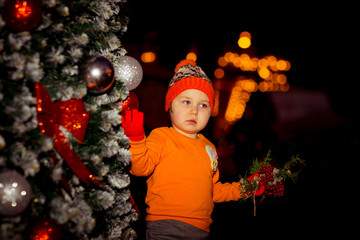 a small, beautiful girl in bright clothes,and in an orange hat, dancing near a Christmas tree, with a Christmas bouquet in her hand