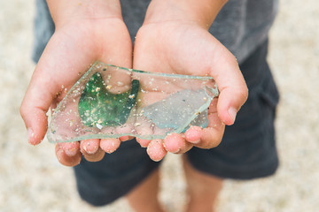 Large pieces of collected sea glass in a young child's sand covered hands.