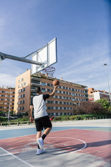 Fototapeta premium On an urban court, strong athlete plays basketball alone with an orange ball