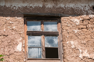 Fototapeta na wymiar Old weathered broken window on neglected adobe clay rural house wall