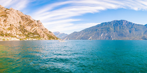 Panorama of amazing Garda lake in Lombardy, Italy surrounded by high dolomite mountains. Boats and yacht floating on the lake. Various hotels and private houses built on the rocky shores of the lake