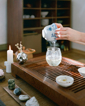 Woman near table pouring tea in pitcher on tea tray at home