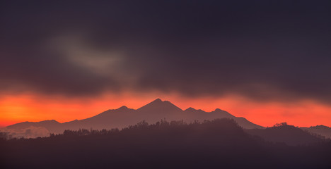 Silhouette of a volcano at sunrise. Red sky and dark clouds. Gunung Rinjani, Indonesia