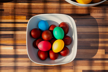 Multicolored Easter eggg in square white bowl on wooden kitchen worktop.