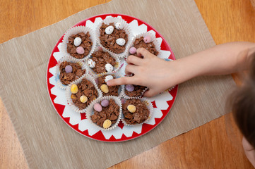 Quickl and gentle loot form plate full of delicious oat chocolate cupcakes decorated with small Easter eggs candies.